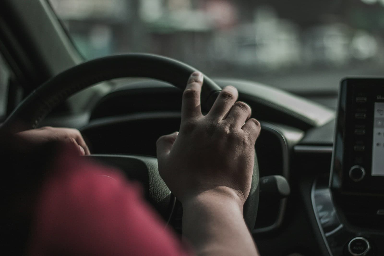 Both hands on a black steering wheel above a modern dashboard