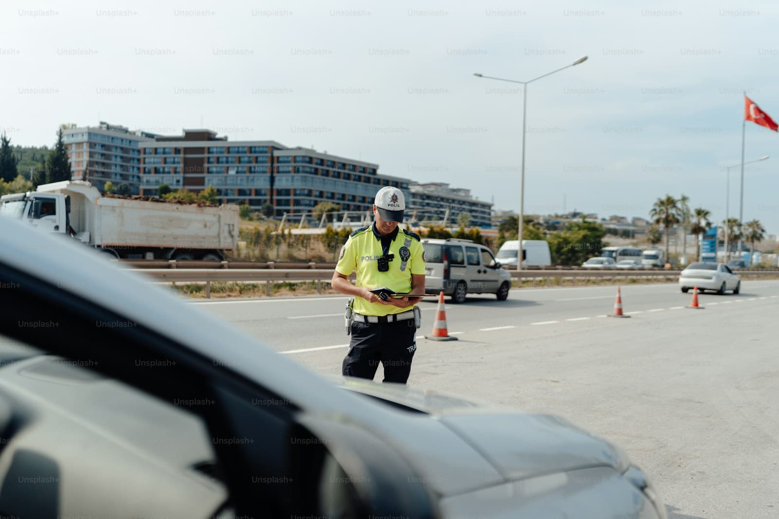 Traffic control worker in safety vest directing traffic on road with orange cones, viewed from inside vehicle
