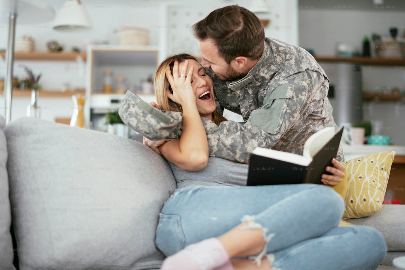 Service member in uniform embracing a woman on a couch in a bright living room