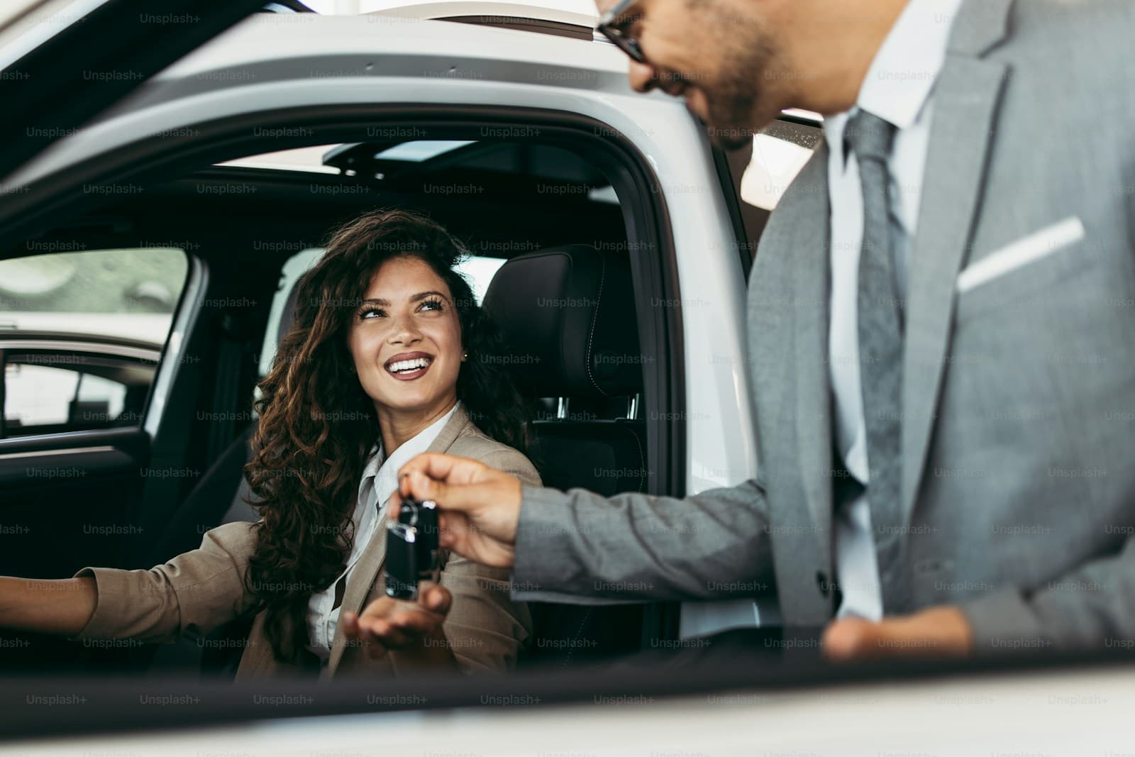 Woman receiving car keys from a man in a gray suit leaning into the open driver's door