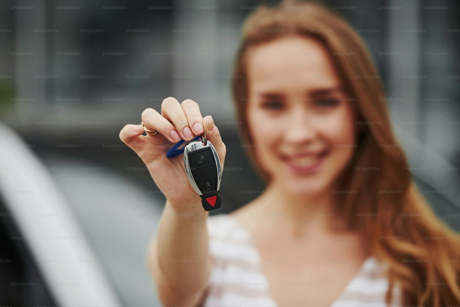 Smiling woman holding car keys toward camera with shallow depth of field