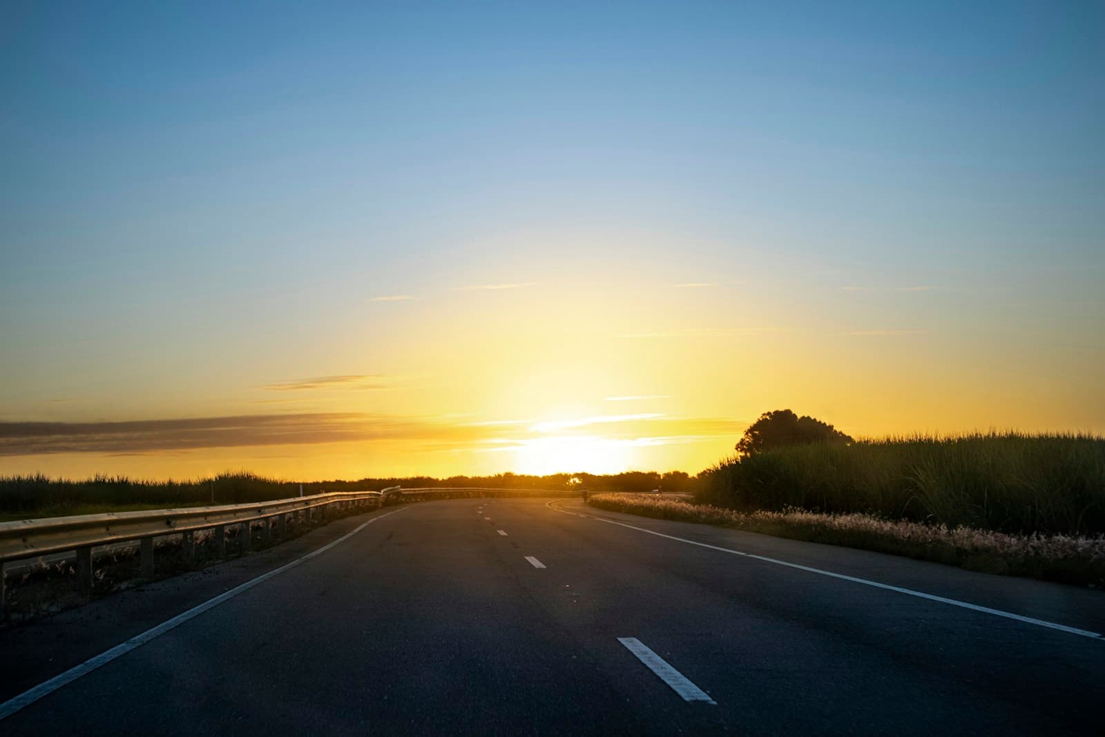 Empty highway road stretching toward bright sun on horizon during golden hour sunset or sunrise