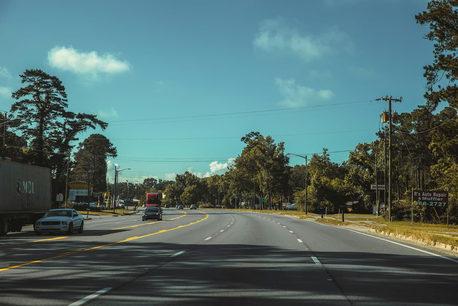 Empty highway road with trees on both sides under blue sky with white clouds