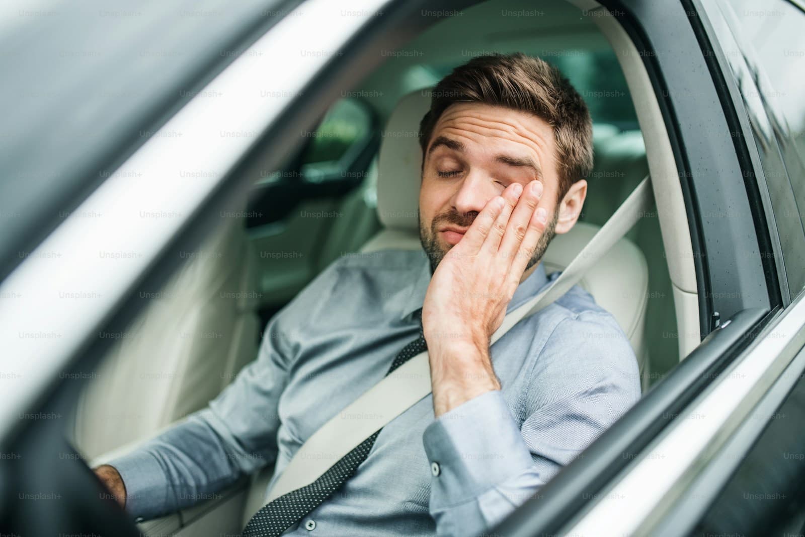Man in a light blue shirt sitting in the driver's seat with his hand over his face
