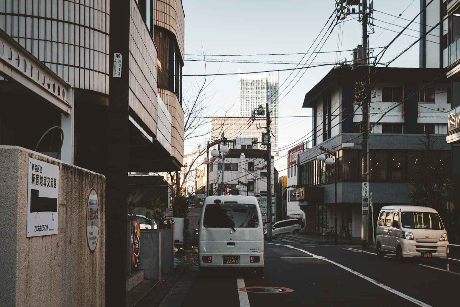 White van and bus on a narrow street lined with multi-story buildings and power lines