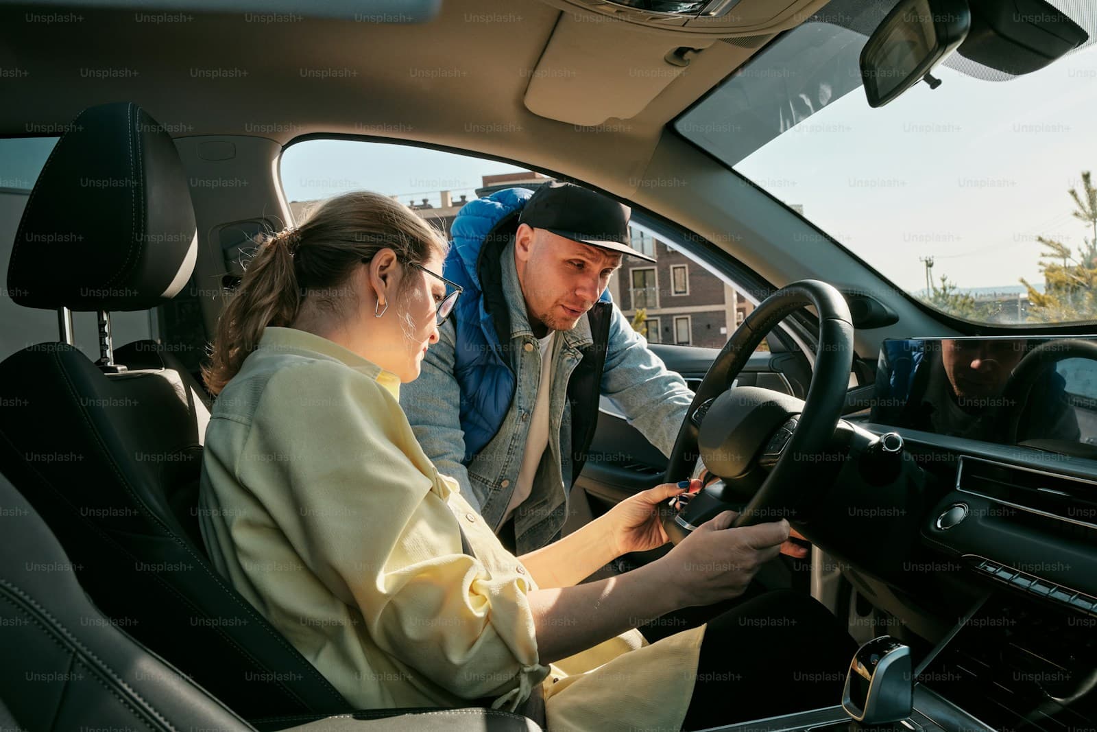 Driving instructor in a blue jacket coaching a young woman seated at the wheel