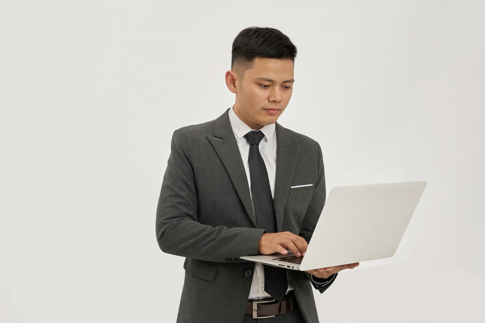 Professional Asian businessman in gray suit using laptop computer against white background